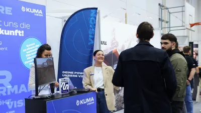 Mehrere Personen stehen vor einem Messestand und unterhalten sich mit den Mitarbeitenden. Halbtotale Einstellung.