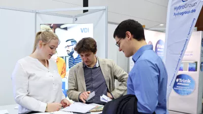 Mehrere Personen stehen an einem Messestand und unterhalten sich. Halbtotale Einstellung.