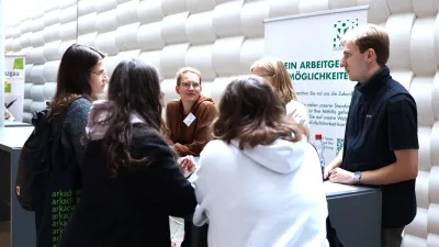 Mehrere Personen stehen an einem Messestand und unterhalten sich. 