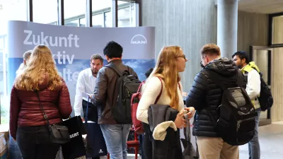 Studierende stehen vor einem Messestand. Halbnahe Einstellung. 