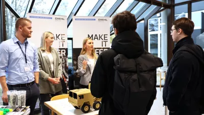 Studierende stehen vor einem Messestand und unterhalten sich mit den Mitarbeitenden. 