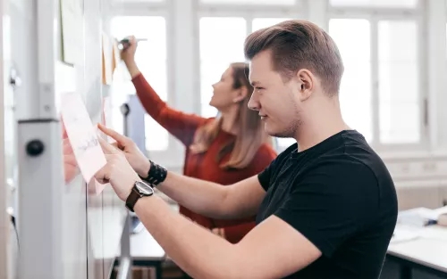 Zwei Studierende schreiben hintereinander auf Flip Charts.