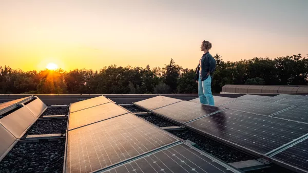 Person steht bei Sonnenuntergang neben Solarpanels auf einem Dach und blickt in die Ferne.