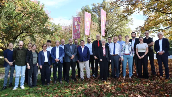 Die Mitglieder des Senats der RWU stehen vor dem Hauptgebäude. Im Hintergrund sind Fahnen mit Logo "60 Jahre RWU" zu sehen. 