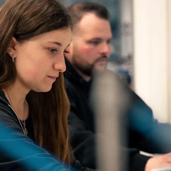 Zwei Studierende in Seitenansicht an Computern, Geräten. 